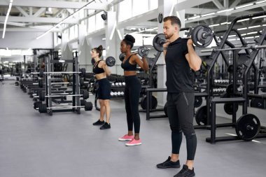 Sportif insanlar ve çok ırklı gruplar spor salonunda ağır toplarla egzersiz yapıyorlar.
