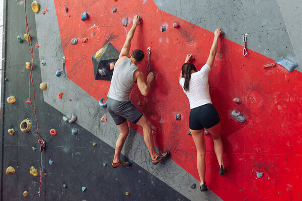 Fit man and woman competing at the climbing wall.