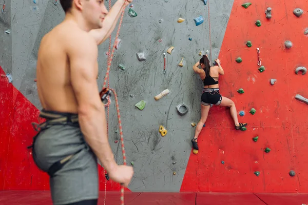 Joven guapo hombre teniendo un descanso en el gimnasio mientras que la chica activa disfrutando de la escalada — Foto de Stock