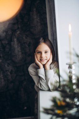 Pencerenin yanında duran küçük kız kameraya poz veriyor.