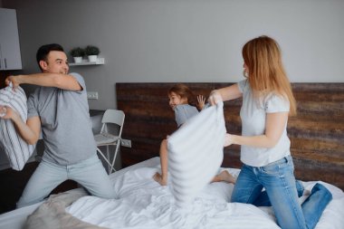 Mutlu ebeveynler ve çocuklar yatakta yastıklarla eğleniyorlar.