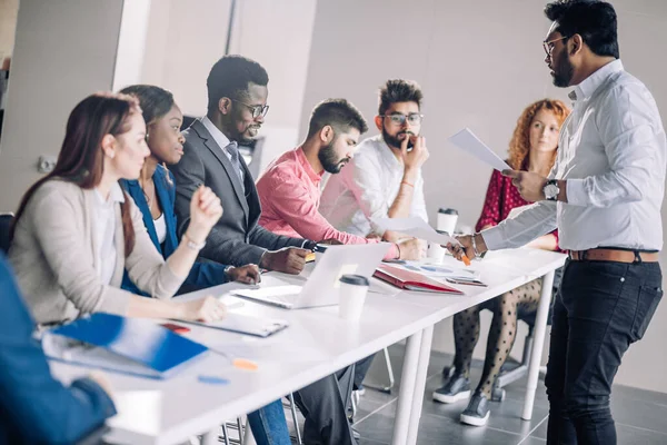 Des gens de race mixte écoutent la présentation assis en rangée à la table de la salle de conférence — Photo