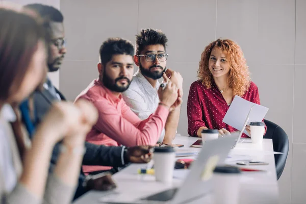 Mixed race people listening to presentation sitting in row at boardroom table