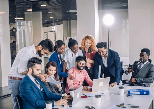 Equipo de trabajo multiétnico joven intercambia ideas reunidas alrededor de computadoras portátiles —  Fotos de Stock