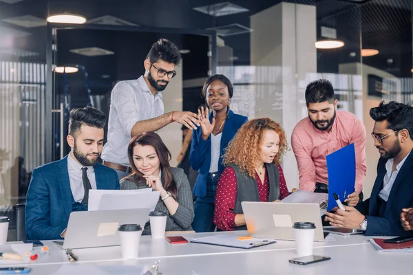 Young multi-ethnic work team exchanges ideas gathering around laptop computers