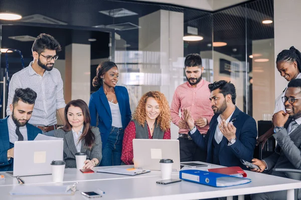 Equipo de trabajo multiétnico joven intercambia ideas reunidas alrededor de computadoras portátiles —  Fotos de Stock