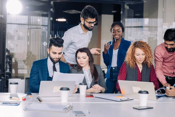 Equipo de trabajo multiétnico joven intercambia ideas reunidas alrededor de computadoras portátiles — Foto de Stock