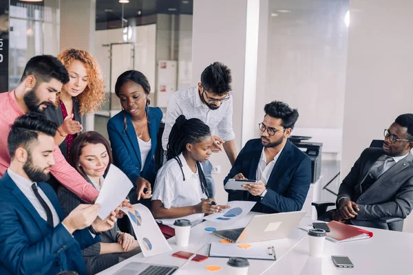 Equipo de trabajo multiétnico joven intercambia ideas reunidas alrededor de computadoras portátiles — Foto de Stock