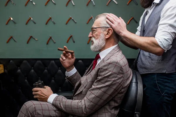 Barbudo viejo hombre de negocios sentado en la peluquería en silla de elegir el diseño de corte de pelo —  Fotos de Stock