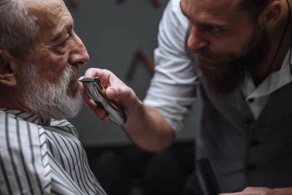 Peluquería haciendo estilo con la máquina de afeitar eléctrica para el anciano en la peluquería —  Fotos de Stock