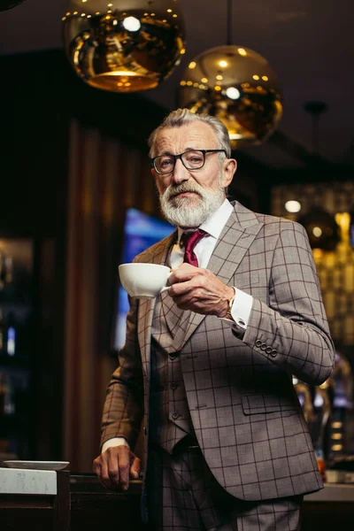 Senior hombre de negocios beber café cerca del mostrador de bar en el interior del restaurante oscuro — Foto de Stock