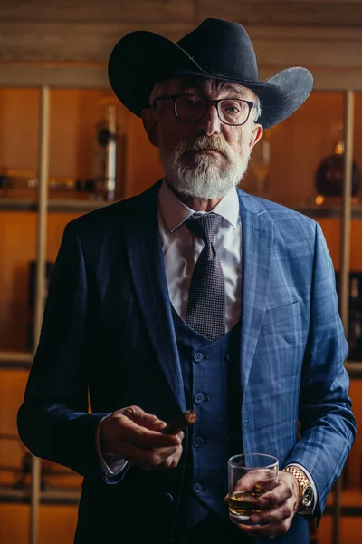 Stijlvolle oude man met brede hoed en rijke blauwe mannen pak rook — Stockfoto