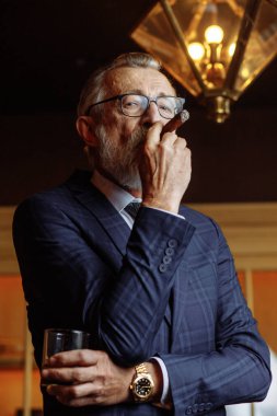 Resmi takım elbiseli yaşlı bir işadamı viski ve puro içiyor.