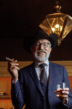 Geniş kenarlı şapkalı şık yaşlı adam ve zengin mavi adam elbisesi dumanı.