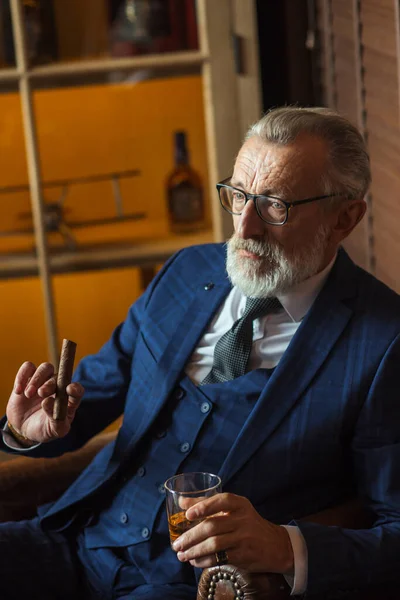 Äldre affärsman med glas whisky och cigarr på mörk bakgrund — Stockfoto