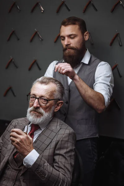 Barbuto vecchio uomo d'affari seduto al negozio di barbiere in sedia scegliendo taglio di capelli design — Foto Stock