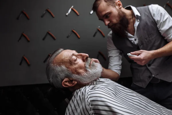 Old man getting his beard shaved by barber