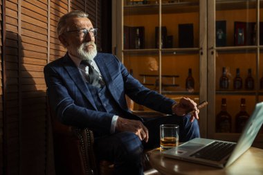 Dizüstü bilgisayara bakan, barda otururken roman yaratan kıdemli bir tiyatrocu..