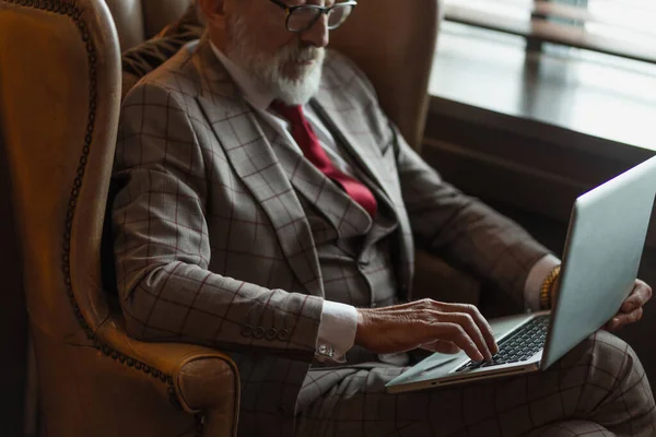 Модный пожилой писатель в элегантной одежде, работающий на ноутбуке. — стоковое фото