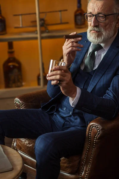 Anciano hombre de negocios con vaso de whisky y cigarro sobre fondo oscuro — Foto de Stock