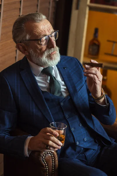 Äldre affärsman med glas whisky och cigarr på mörk bakgrund — Stockfoto