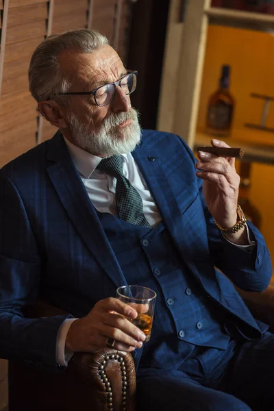 Anciano hombre de negocios con vaso de whisky y cigarro sobre fondo oscuro — Foto de Stock