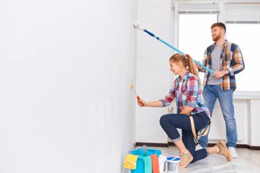 Kareli gömlekli bir çift birlikte duvar boyuyor. DIY yenileme konsepti.