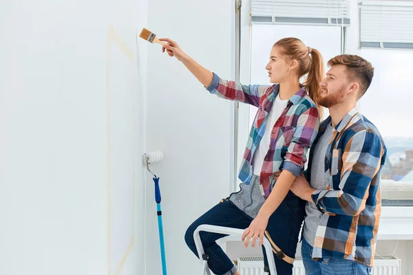 Paar in lässigen karierten Hemden bemalen Hauswand zusammen. DIY-Sanierungskonzept. — Stockfoto