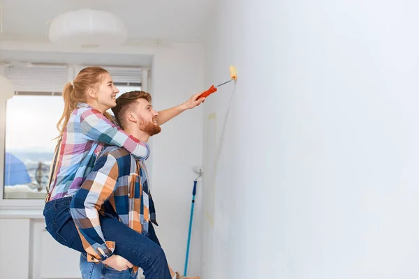 Woman piggybacking on her husband to gain extra height when painting home wall — Stock Photo, Image