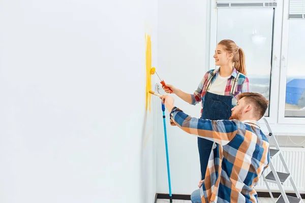 Paar in lässigen karierten Hemden bemalen Hauswand zusammen. DIY-Sanierungskonzept. — Stockfoto