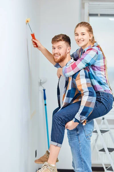 Jong stel schilderen muren in hun nieuwe huis, meeliften en plezier hebben. — Stockfoto