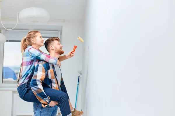새로운 집에 벽을 페인트칠하고 있는 젊은 부부 , 피이 백 하고 재미있게 놀고 있다. — 스톡 사진