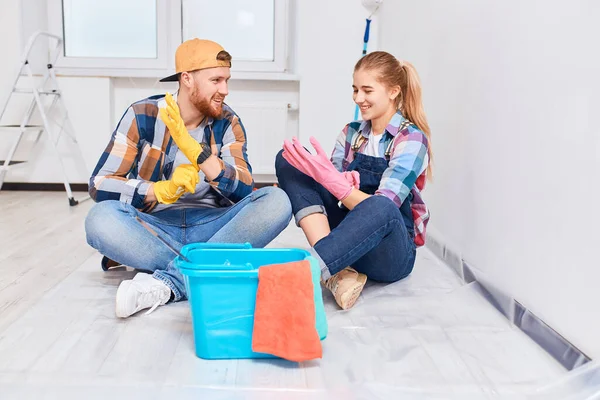 Paar klaar om te schilderen, zitten op de vloer, het aantrekken van rubberen handschoenen — Stockfoto