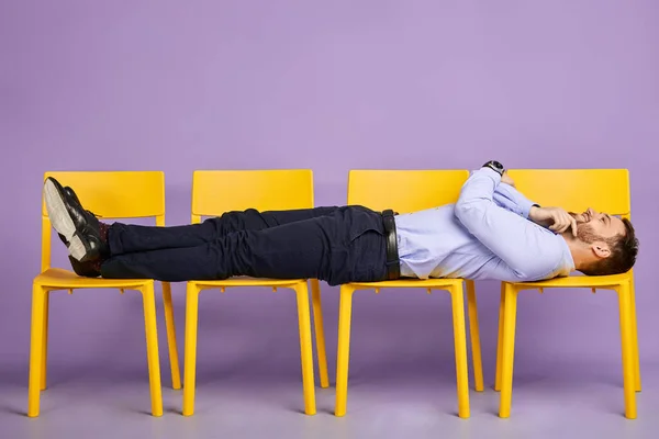 Jonge man liggend op gele stoelen naar boven kijkend — Stockfoto