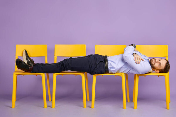 young man laying down on yellow chairs looking in camera