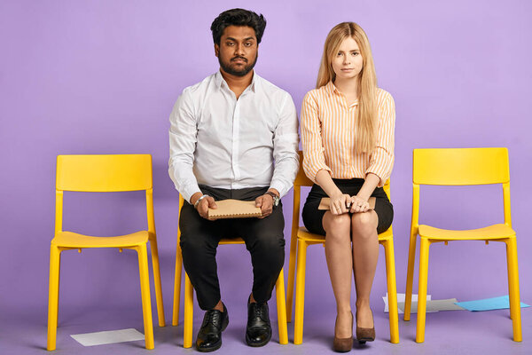dark-skinned man and blonde woman sitting on chairs