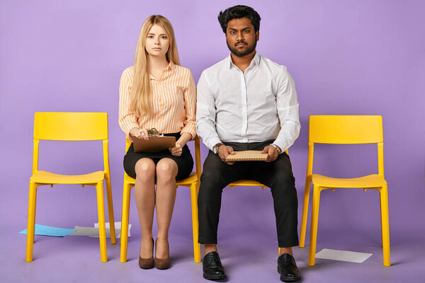 dark-skinned man and blonde woman sitting together on chairs
