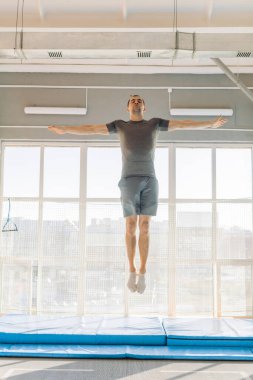 Genç yakışıklı adam trambolinde zıplamaktan zevk alıyor.