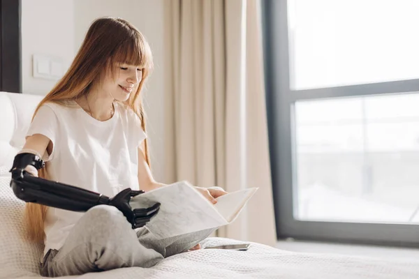 Close-up photo of a beautiful girl holding a book with an artificial arm. — Stock Photo, Image