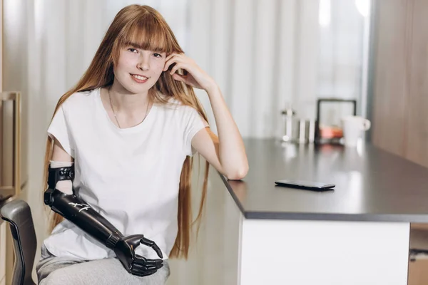 Ehrfürchtiges Mädchen mit einem Cyber-Arm, der sich auf den Tisch lehnt und in die Kamera schaut — Stockfoto