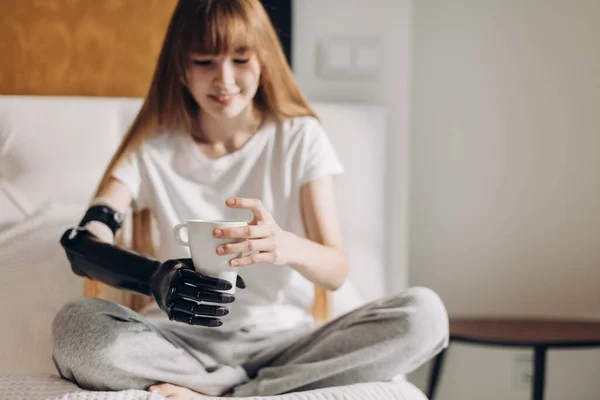 Улыбающаяся девушка с протезной кибер-рукой, держащая чашку — стоковое фото