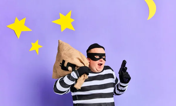 Aufgeregter, gerissener, pummeliger Häftling in gestreifter Kleidung mit Geldbeutel und Pistole auf blauem Hintergrund. Porträt aus nächster Nähe. — Stockbild Fette Gefangene mit Geldbeutel und Waffe auf der Flucht vor der Polizei — Stockfoto