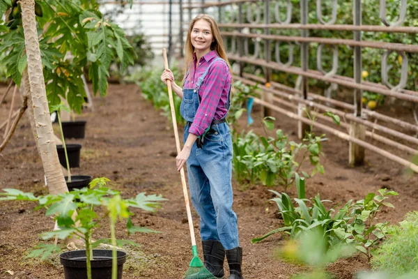 Chica con estilo en camisa a cuadros y de pie general con un rastrillo en el jardín — Foto de Stock