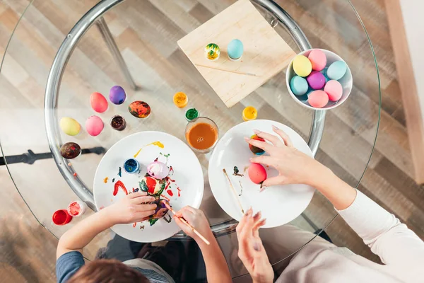 Top view of woman and child painting Easter eggs over wooden background — Stock Photo, Image