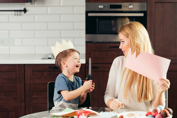 Madre e hijo cortando papel con tijeras en casa, preparando la decoración de Pascua. — Foto de Stock