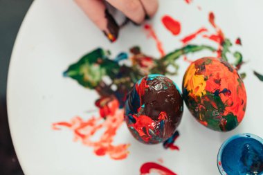 Bir çocuk tarafından boyanmış, beyaz tabağa yerleştirilmiş Paskalya yumurtalarının üst görüntüsü..