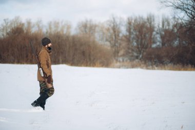 Erkek giysileri, av tüfeğiyle sahada yürüyor.