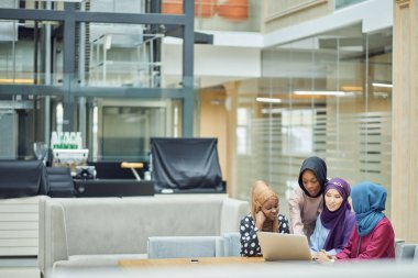 Kafede dizüstü bilgisayar kullanan, başörtüsü ve başörtüsü takan Müslüman Asyalı ve Afrikalı kadınlar