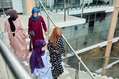 Alışveriş merkezinin merdivenlerinde yürüyen dört Müslüman kız grubu.