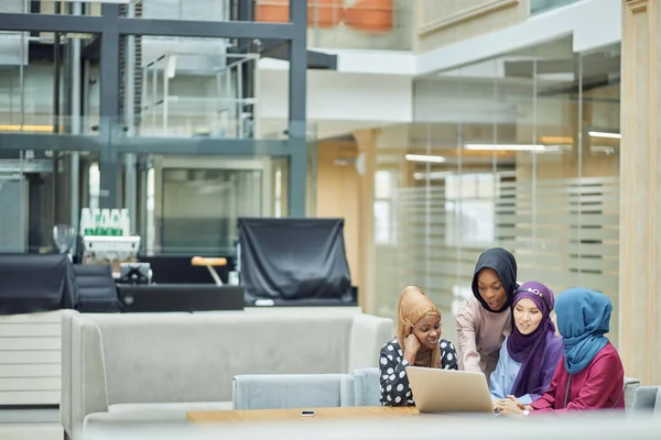 Kafede dizüstü bilgisayar kullanan, başörtüsü ve başörtüsü takan Müslüman Asyalı ve Afrikalı kadınlar